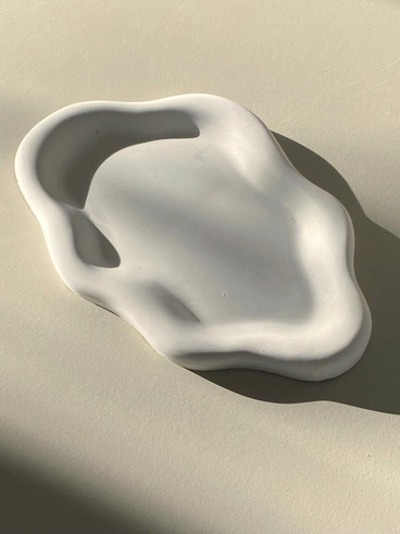A softly irregular white decorative tray lit by afternoon sun